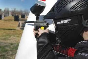 man aiming paintball gun behind obstacle