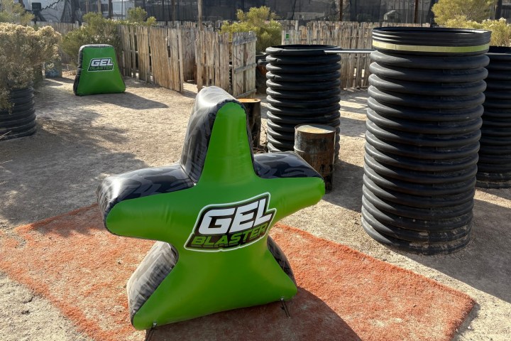 Outdoor paintball field with inflatable green star barriers labeled 'Gel Blaster' and cylindrical cover.