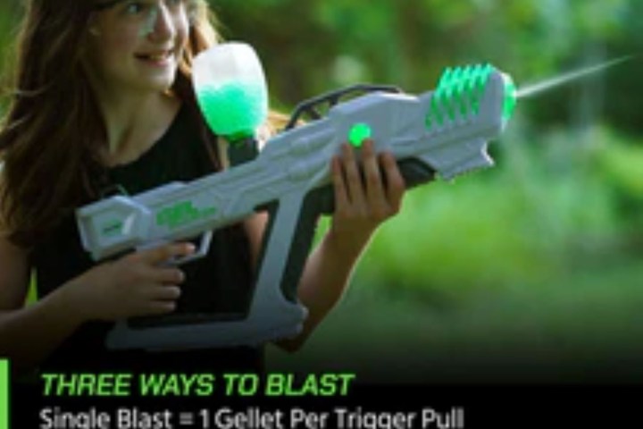 Girl wearing goggles holding a large toy gun with glowing green parts, standing outdoors.