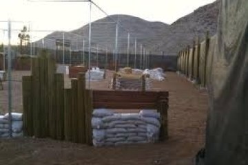 Outdoor paintball field with bunkers and netting, mountains in the background.