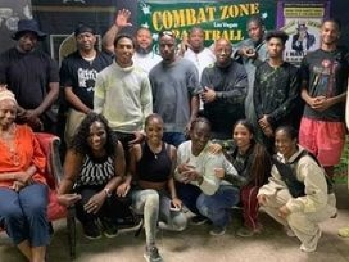 Group of people posing together indoors in front of a 'Combat Zone Paintball' sign.