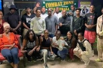 Group of people posing together indoors in front of a 'Combat Zone Paintball' sign.