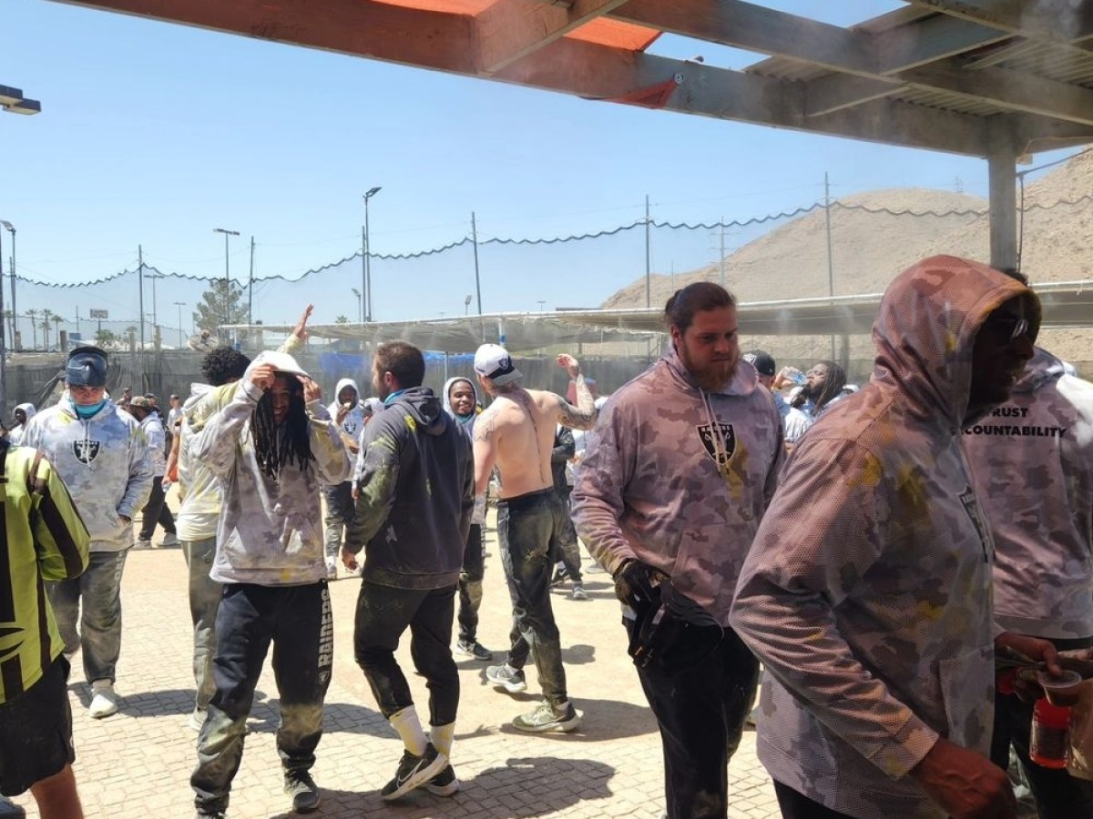 Group of people in casual clothing enjoying outdoor paintball game under a shelter.
