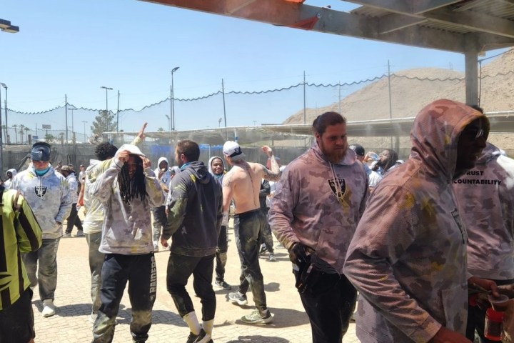 Group of people in casual clothing enjoying outdoor paintball game under a shelter.