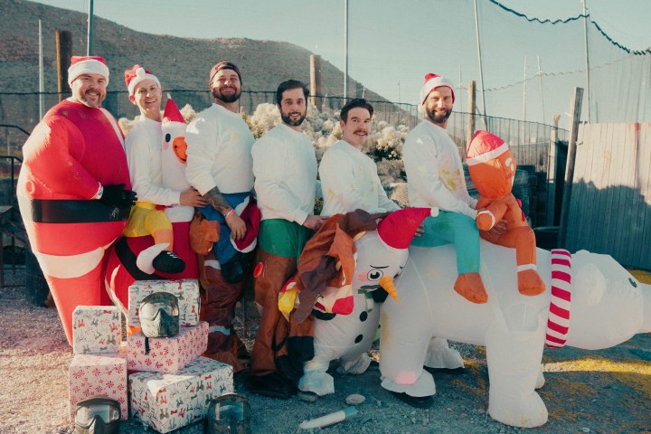 Group of six people wearing inflatable Christmas costumes with gift boxes outdoors on a sunny day.