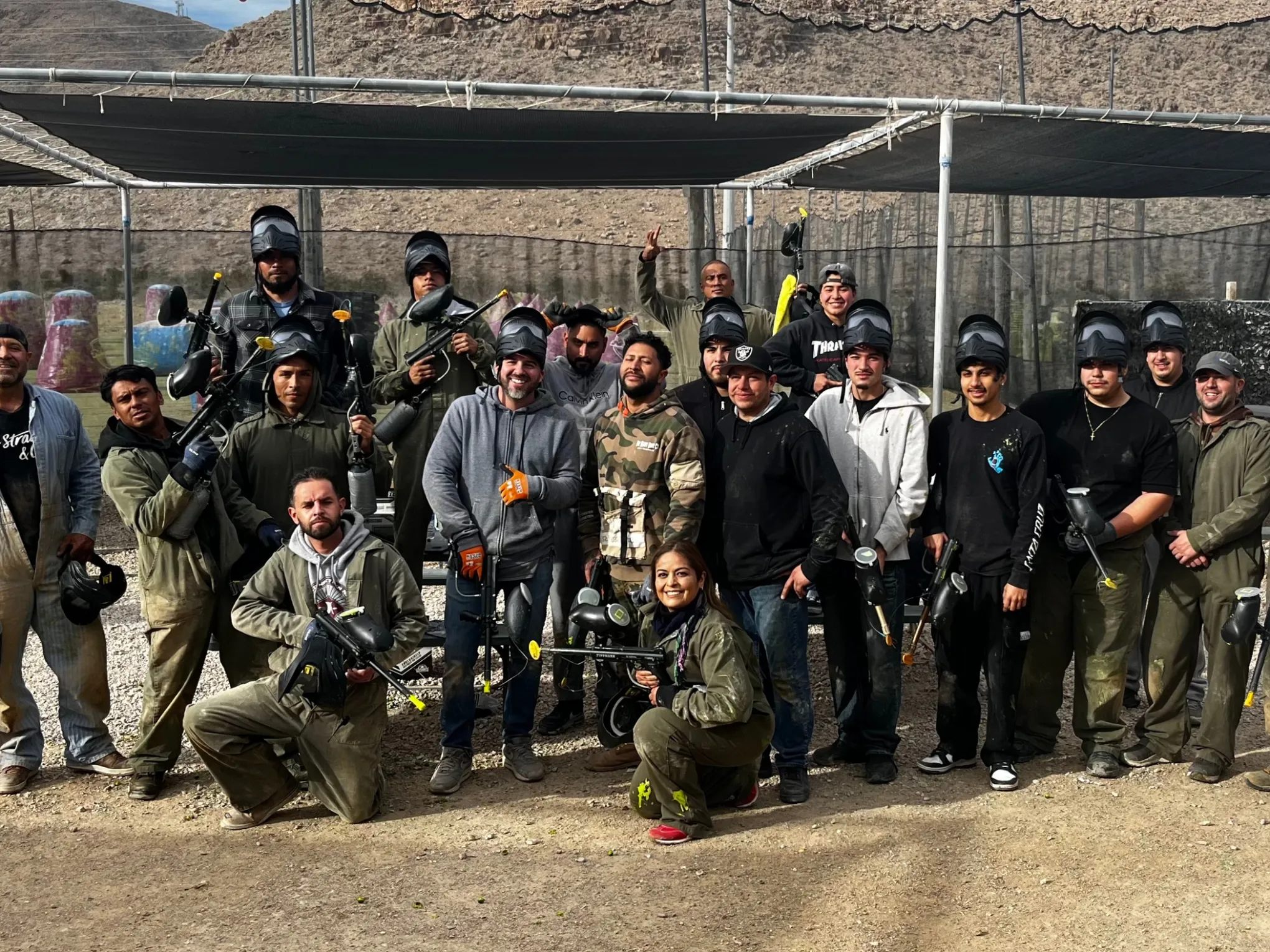 Group of people posing with paintball gear at an outdoor field.