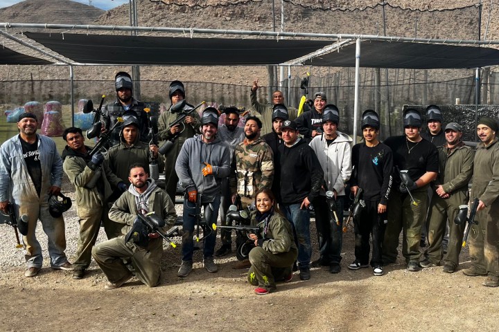 Group of people posing with paintball gear at an outdoor field.