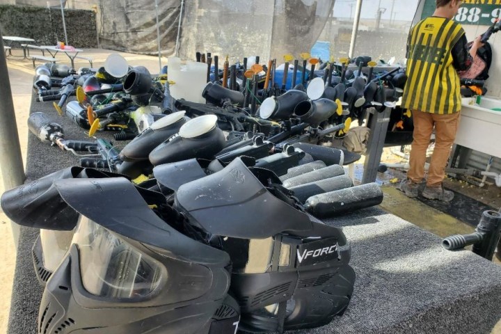 Paintball masks and guns on a table, person cleaning equipment in the background.