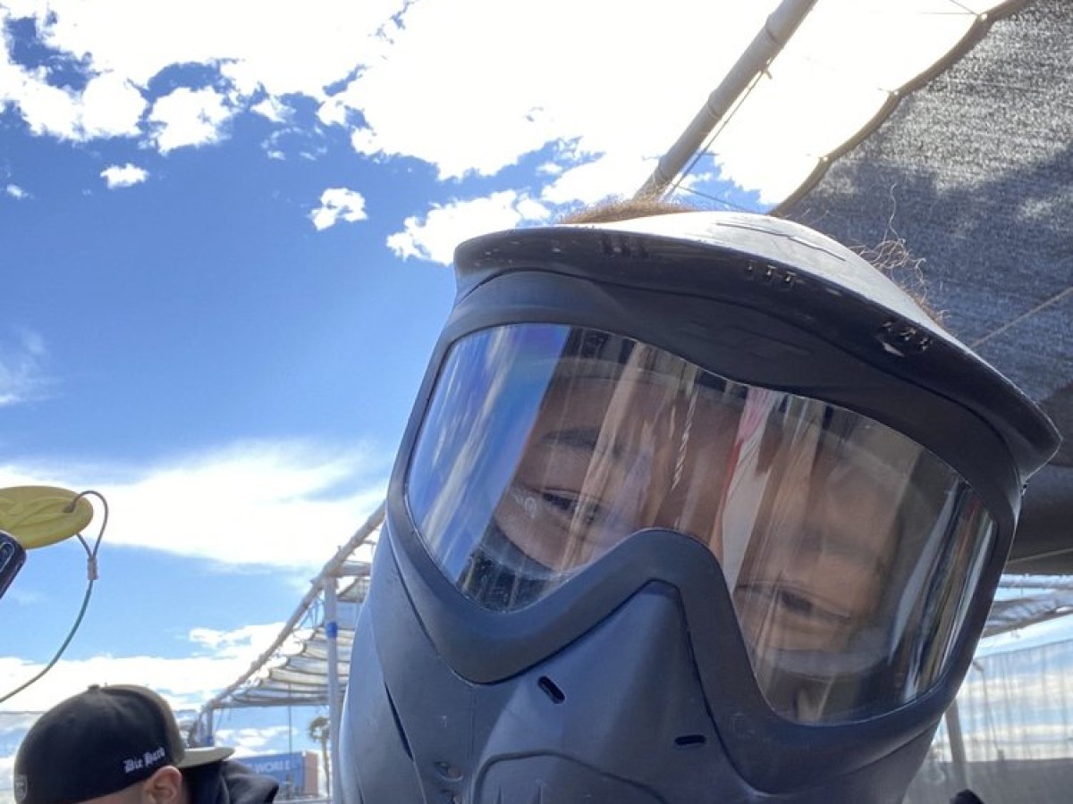 Person wearing a paintball mask outdoors, with another person in the background.